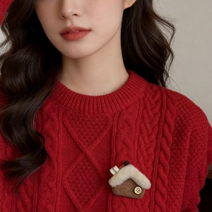 Detail of creative house-shaped felt brooch with sheep-like fur on a red cable knit sweater