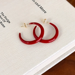 Macro detail of red enamel C-shaped hoop earrings on a minimalist white book cover