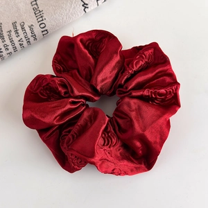 Detail of dark red satin scrunchie with embossed rose floral texture on white background
