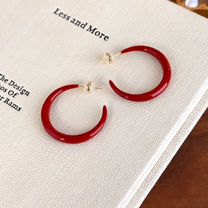 Close-up of red enamel C-shaped earrings with gold needles on a book background