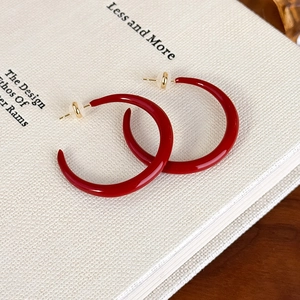 Close-up of deep red enamel hoop earrings with golden ball backings on a book surface