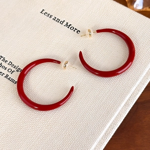 Detail of red enamel C-shaped earrings with gold pins on a minimalist fabric book