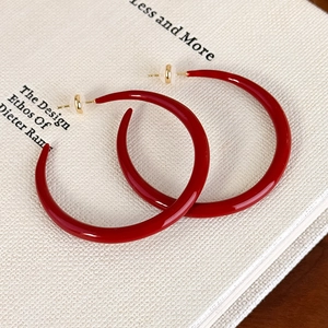 Close-up of red enamel C-shaped hoop earrings with gold pins on a white book surface