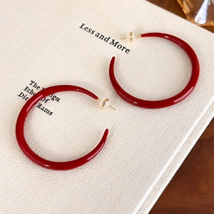 Macro shot of red enamel C-shaped hoop earrings with gold pins on a book cover