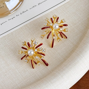 Macro view of gold fireworks earrings with red enamel petals and center pearl detail