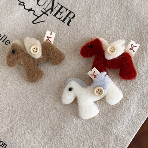 Detailed view of three plush pony brooches in brown, red, and white with button wings
