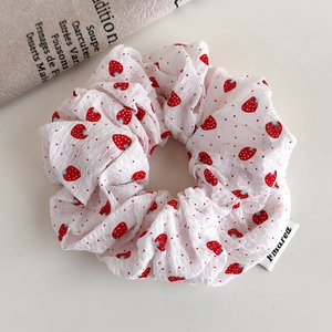 Detail of white strawberry print scrunchie with brand label and vintage linen backdrop