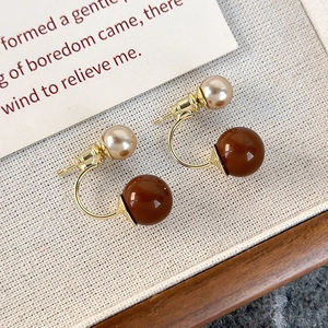 Dettaglio di orecchini vintage con sfera marrone ambrata e perla color champagne