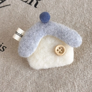 Close-up of handmade wool felt house brooch with wood button and blue pom-pom on linen
