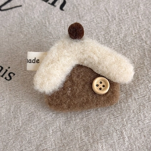 Detailed view of handmade felt house brooch with wood button and plush roof on linen fabric