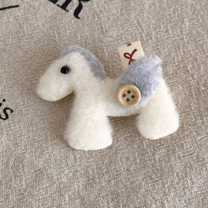Detailed macro view of cream felt pony brooch with wooden button and wings on linen