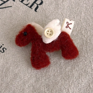 Macro detail of a plush horse brooch with felt wings, wooden button and fabric tag