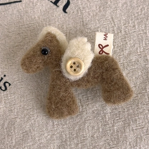 Macro detail of handmade felt flying horse brooch with a wooden button on linen fabric