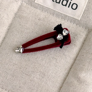 Close-up of red velvet heart hair clip with black bow and sparkling rhinestone details