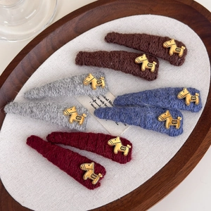 Knitted ponytail hair clips with gold horse charms in autumn colors on a wooden tray