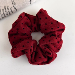 Detailed view of plush burgundy scrunchie with black polka dots on vintage paper