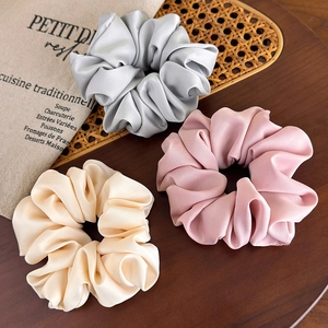 Three satin scrunchies in silver, pink, and beige displayed on a rustic wooden table