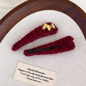 Detail of burgundy knit hair clips with golden horse charm on textured fabric background
