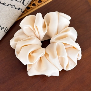 Close-up of silky cream satin scrunchie showing smooth texture on rustic wood