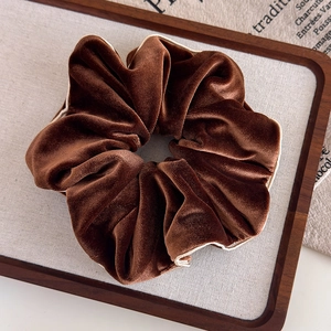 Détail d'un chouchou en velours marron foncé avec liseré beige sur plateau en bois