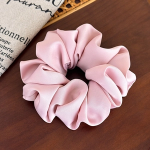 Detailed macro shot of a silky pink satin scrunchie on a vintage wooden surface