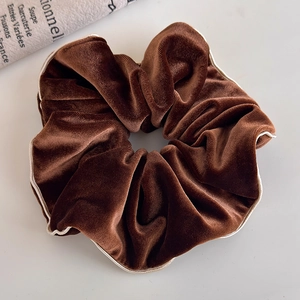 Détail d'un chouchou en velours marron foncé avec des bords ondulés blanc crème élégants