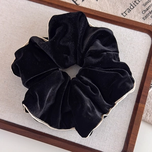 Détail de chouchou en velours noir avec bordure blanche sur un plateau en bois
