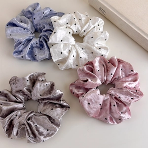 Detailed view of four velvet polka dot scrunchies in pastel colors on a minimal desk