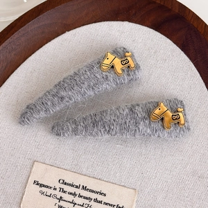 Close-up of grey plush hair clips with gold horse charms on a textured fabric background