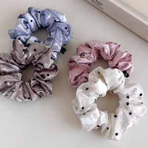 Detailed view of four velvet polka dot hair scrunchies in pastel colors on a minimal desk