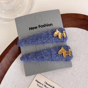 Close-up of blue plush hair clips with gold horse charms on a textured display card
