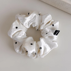 Detail of cream velvet scrunchie with black polka dots and minimalist black woven tag