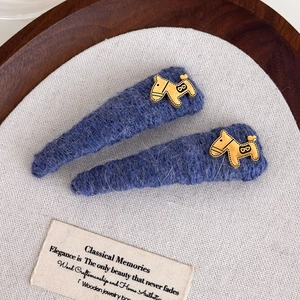 Detail of navy blue knitted hair clips with golden horse charm on grey linen