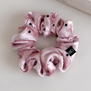 Close-up of pink velvet polka dot scrunchie with brand label on a white background