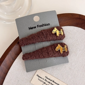 Detailed macro view of dark brown knitted hair clips with golden pony charms on card