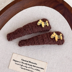 Detail of dark brown knit hair clips with golden pony charms on a vintage wooden tray