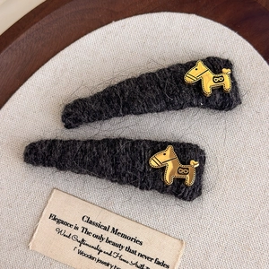 Detail of dark grey knitted hair clips with golden horse motifs on a vintage background
