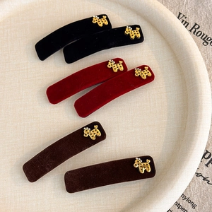 Detail view of velvet hair clips with gold poodle charms and rhinestones on a white plate