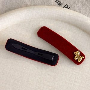 Macro view of red velvet hair clips set with gold horse emblem on a textured tray