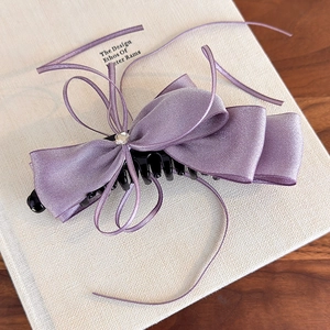 Détail du nœud en satin violet avec cristal et pince banane sur fond de livre