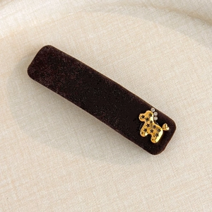 Macro detail of dark brown flocked hair clip with golden poodle and star hollowed design