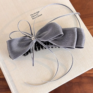 Détail d'une pince à cheveux en satin gris avec nœud et cristal posée sur un livre