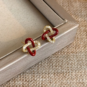 Close-up of interlocking red enamel and gold zircon knots on a luxury stud earring