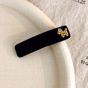 Macro shot of black velvet hair clip with gold dog emblem on a textured surface