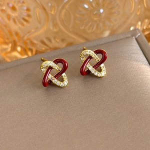 Macro detail of gold-plated knot earrings with red enamel and pavé zircon stones