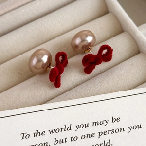 Close-up of red velvet bow pearl earrings displayed in a soft beige jewelry box