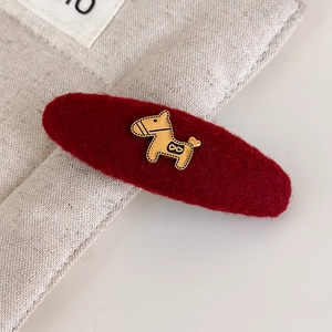 Detailopname van een rode vilten haarclip met een goudkleurige metalen paardenhanger