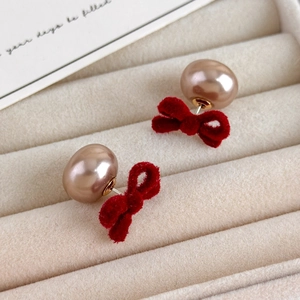Macro detail of red velvet bow and champagne pearl earrings in a beige velvet jewelry box