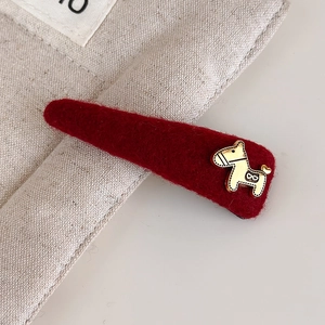 Close-up van een rode vilten haarclip met een gouden pony-embleem en hartdetail