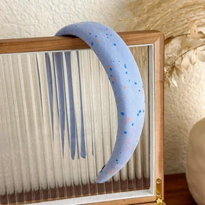 Detailed macro view of light blue padded fabric headband with colorful paint splatters